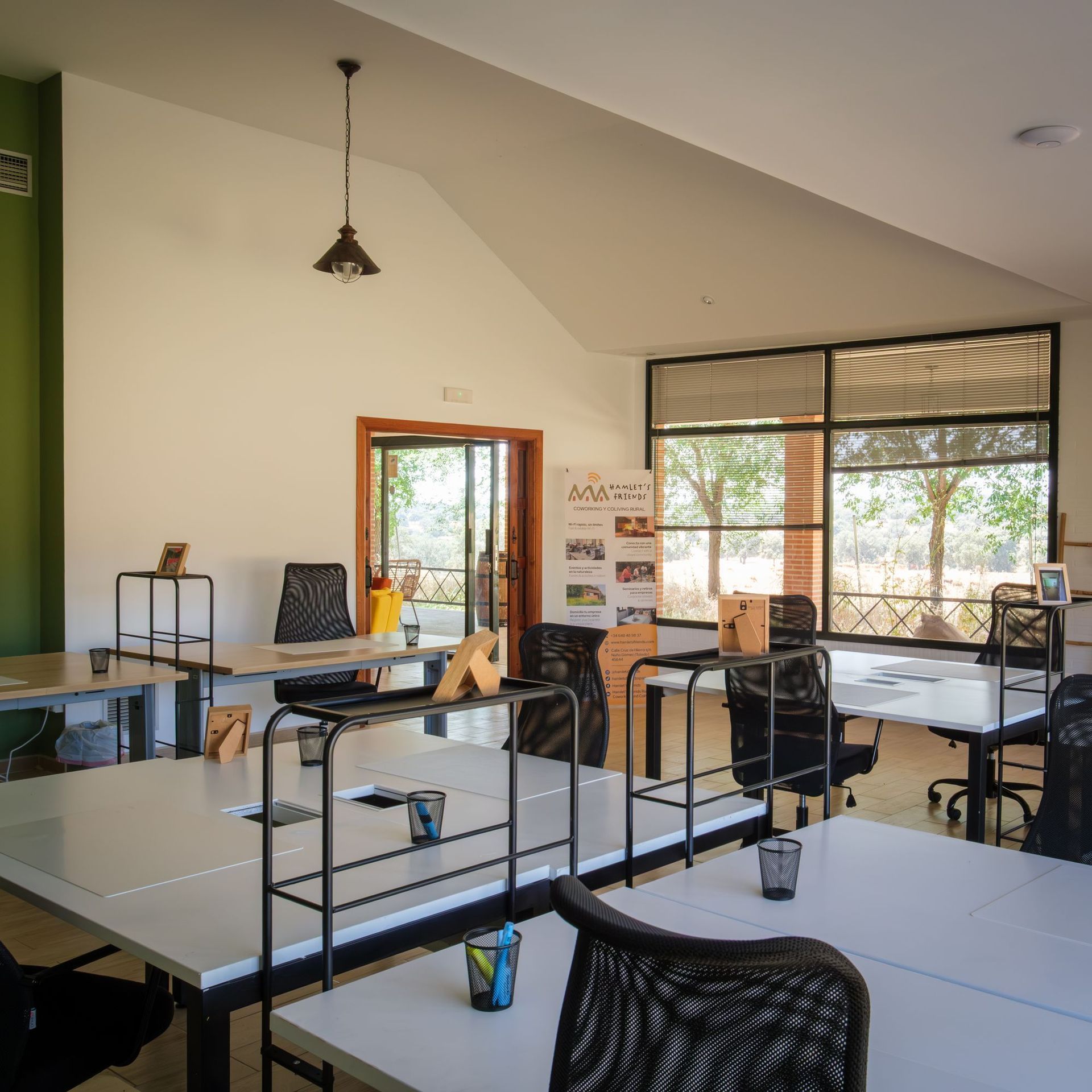 Desks and ergonomic chairs in the 200 m² coworking space at Hamlet's Friends, a converted golf clubhouse with floor-to-ceiling windows onto the dehesa